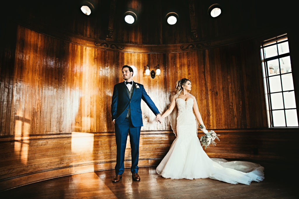 Photograph of bride and groom holding hands and looking away from each other in a grand wood paneled room at Powel Crosley Estate as an example of a historic Central Florida wedding venue